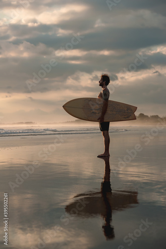 Athletic surfer stands at serene evening beach