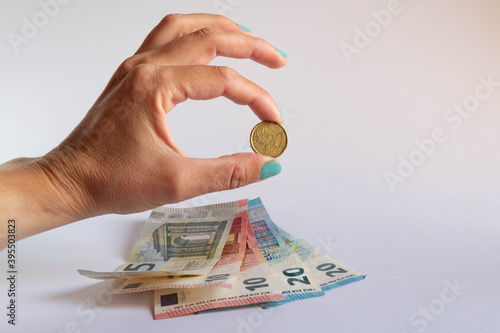 Hand holding a 20 cent coin over some euro bills on white background