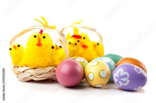Yellow chickens in straw baskets. Easter decoration. Painted easter eggs in foreground. Studio photo isolated on white background. Selective focus.
