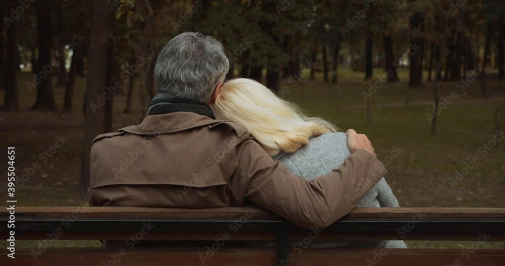 Senior husband hugging wife, happy couple sitting together on bench in park Senior husband hugging wife, happy couple sitting together on bench in park