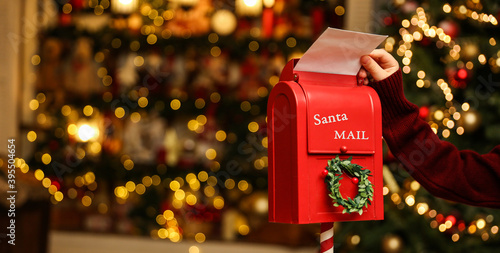 Photo Child's hand puts a letter to santa claus in the christmas mailbox