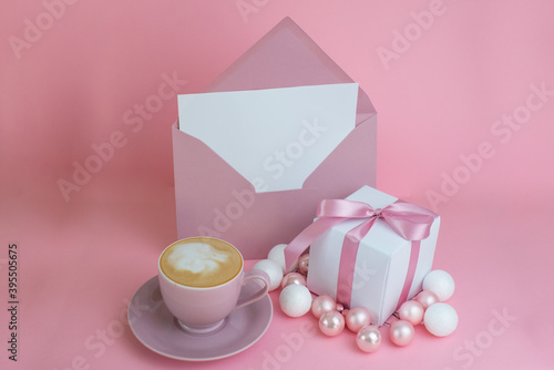 A pink gift, an empty envelope and a pen. Letter to St. Nicholas. Women's Christmas. Gift or present box with shiny balls, ribbons and snowflakes on pink background. Flat lay composition for christmas