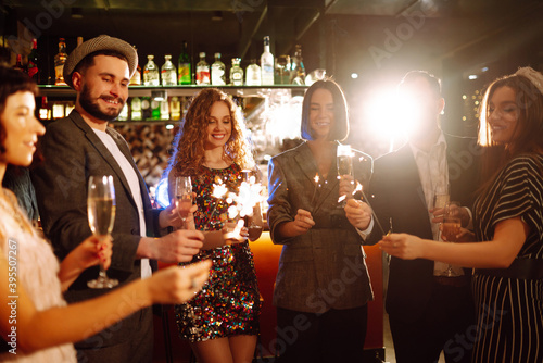 Group of happy people holding sparklers at the party. Young friends clinking glasses of champagne and enjoying new years eve with fireworks. Party  celebration  holidays concept.