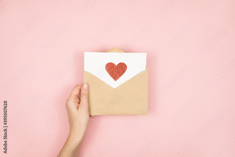 Obraz premium Love letter in women hands on Valentines Day. Handmade postcard with red heart on pink background. 14 February concept