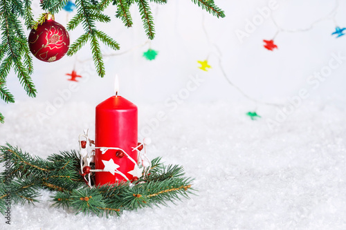 New Year's, Christmas red candle surrounded by branches of green spruce on artificial snow. Green spruce branch decorated with New Year's toys.