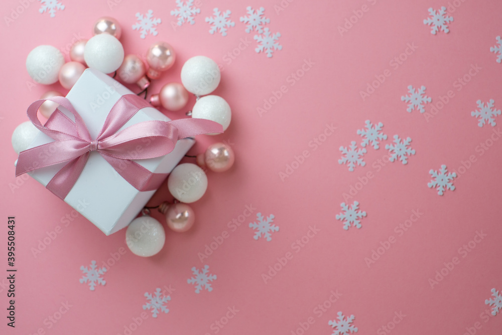 Fototapeta premium Gift or present box with shiny balls, ribbons and snowflakes on pink background. Flat lay composition for christmas, female Christmas. White gift with pink ribbons. A gift box isolated on pink 