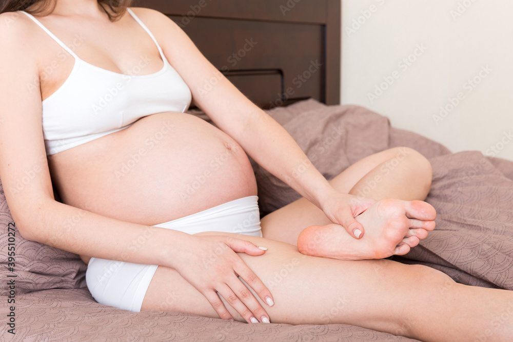 Pretty pregnant woman hands massaging leg sitting on bed