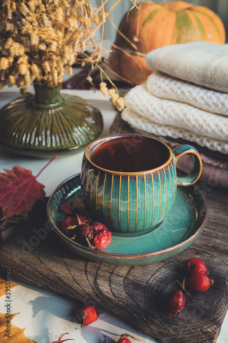 Cup of tea or coffee with a teapot in an autumn still life. Beautiful Cup and saucer on a wooden Board surrounded by autumn leaves, on the background of a ripe orange pumpkin