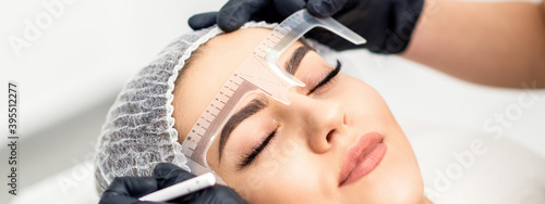 Beautician is measuring the brows with ruler before tattooing eyebrows photo
