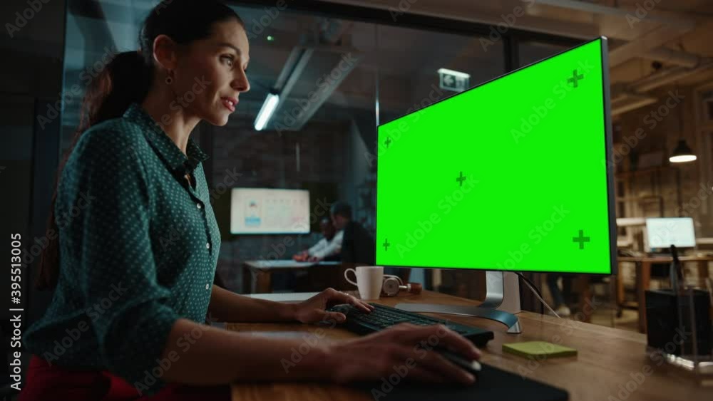 Middle Aged Multiethnic Specialist Working on Desktop Computer with Green Screen Mock Up Display in Busy Creative Office. Beautiful Diverse Female Manager in Green Polka Dot Blouse. Middle Aged Multiethnic Specialist Working on Desktop Computer with Green Screen Mock Up Display in Busy Creative Office. Beautiful Diverse Female Manager in Green Polka Dot Blouse.
