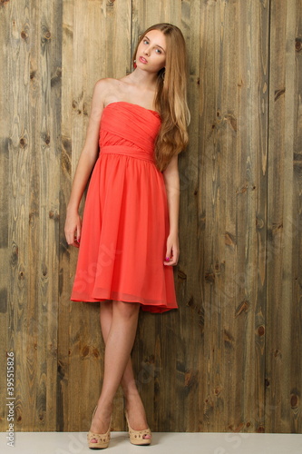 beautiful slender blonde girl in a light red dress near a wooden wall