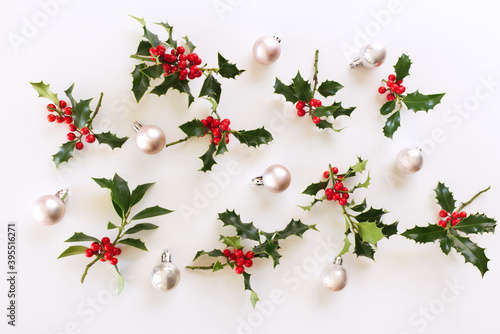 Christmas composition. White decorations and holly branches on white background. Christmas, winter, new year concept. Flat lay, top view, copy space.