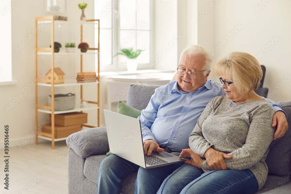 Senior man and woman sitting on sofa in living room watching movie on laptop together.