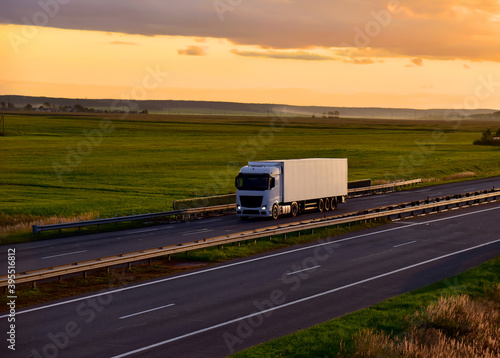 Truck with semi-trailer driving along highway on the sunset background. Goods delivery by roads. Services and Transport logistics. Soft focus.