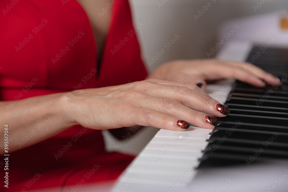 Close-up, female hands on the keys of the piano. On the background of a red dress.