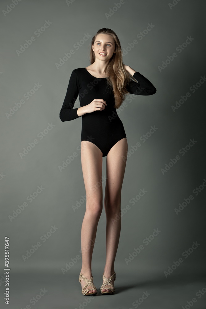 beautiful slender long-legged blonde model in a sports bodysuit posing in  the studio on a gray background. Stock Photo | Adobe Stock