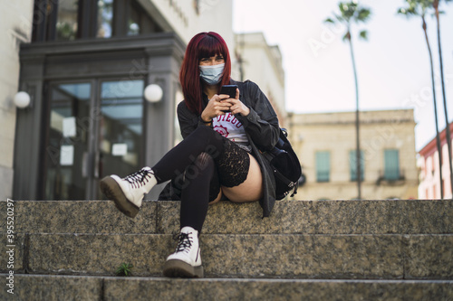 Selective focus shot of an attractive female wearing a facial mask with a phone in her hands photo