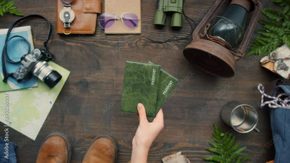 Top view flat lay shot of unrecognizable woman putting two passports on wooden table with travel accessories lying on it Top view flat lay shot of unrecognizable woman putting two passports on wooden table with travel accessories lying on it