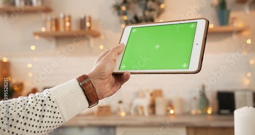 Canvas Print Close up shot of male Caucasian young hand holding tablet with green screen with tracking motion at decorated home