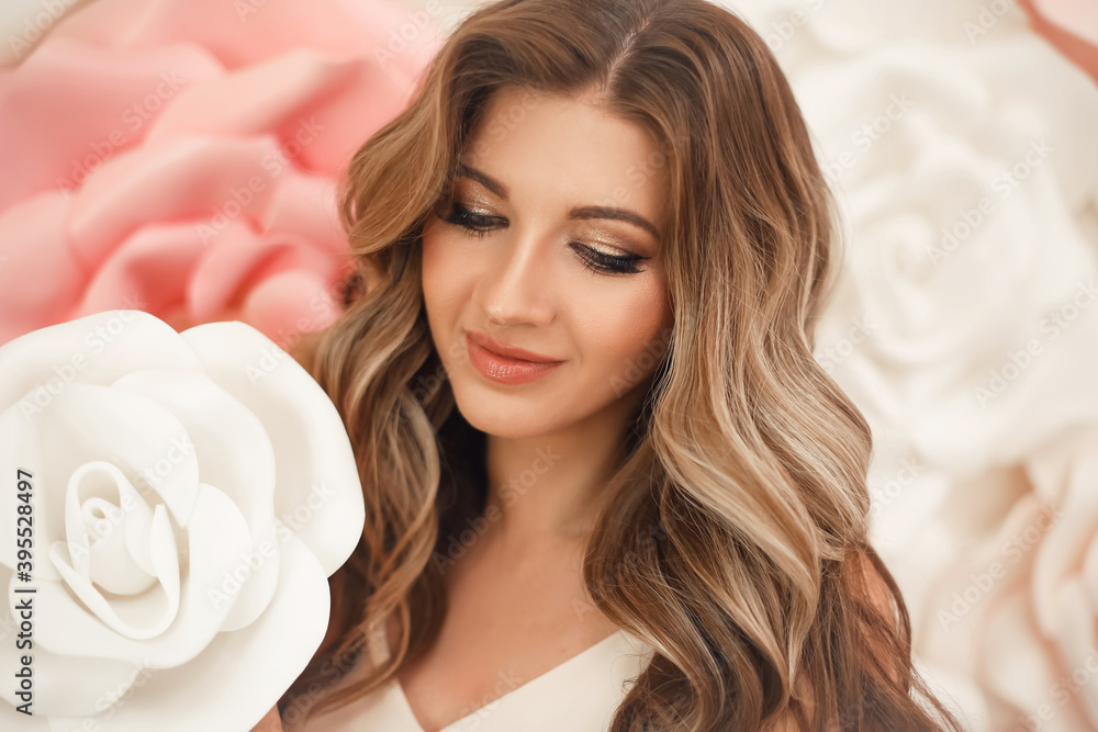 Naklejka premium Beautiful hair. Woman beauty portrait smiling with makeup and long healthy hairstyle over pink white roses flowers.