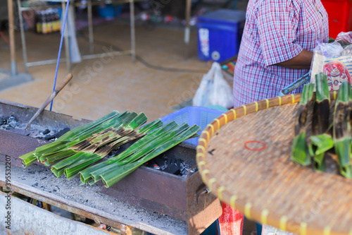 old lady make sweetmeat made of flour coconut and sugar wrapped with banana leaf grill on charcoal Thai dessert