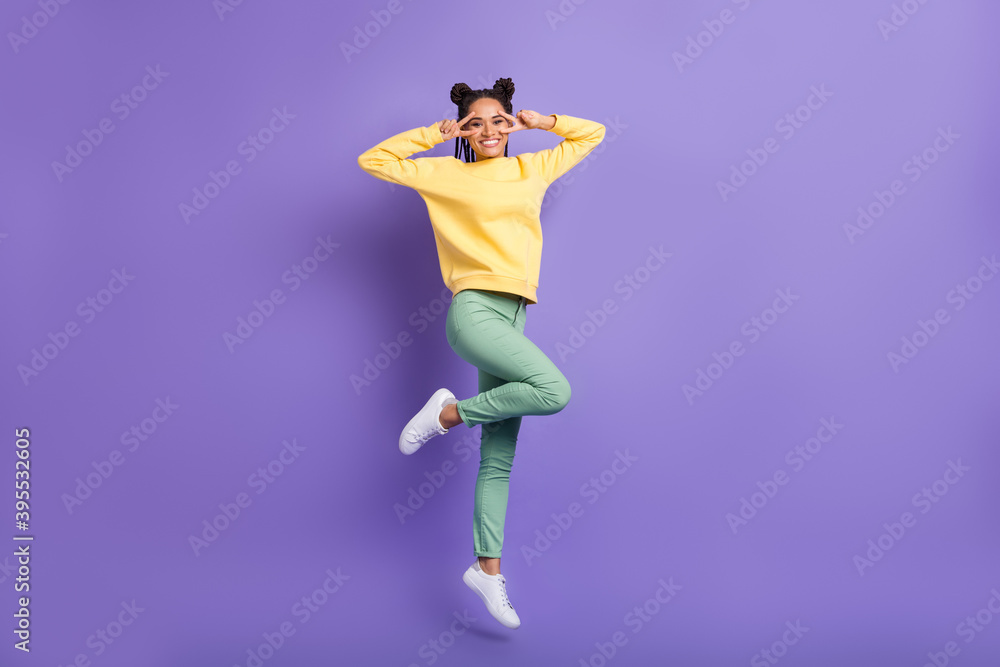 Full size profile photo of optimistic girl jump show v-sign wear yellow shirt trousers sneakers isolated on lilac color background Full size profile photo of optimistic girl jump show v-sign wear yellow shirt trousers sneakers isolated on lilac color background