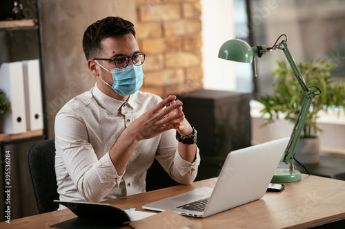 Young businessman with a mask working in his office on laptop. Businessman having video call. COVID - 19 virus protection.