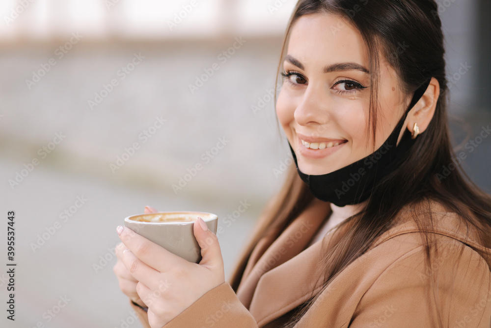 Portraitf of Beautiful woman takes off protective mask for drinking coffee. Female sitting outdoors on terrace and drink coffee during Quarantine, self distancing Portraitf of Beautiful woman takes off protective mask for drinking coffee. Female sitting outdoors on terrace and drink coffee during Quarantine, self distancing