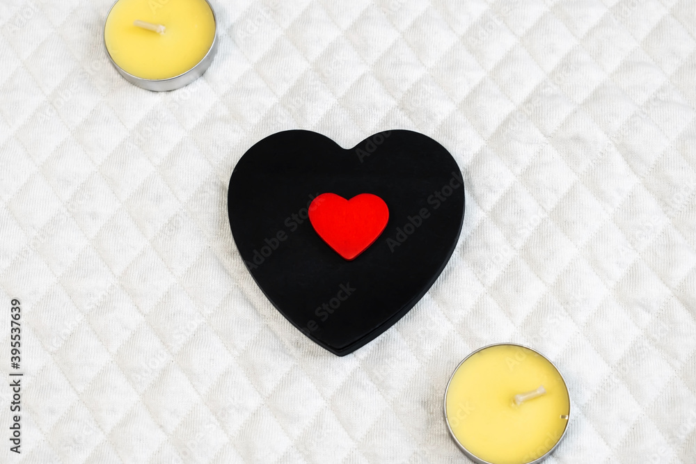 Obraz premium A small red heart is located on a black heart that lies on a white surface next to the candles.