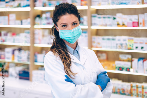 Female pharmacist with protective mask on her face working at pharmacy. Medical healthcare concept.