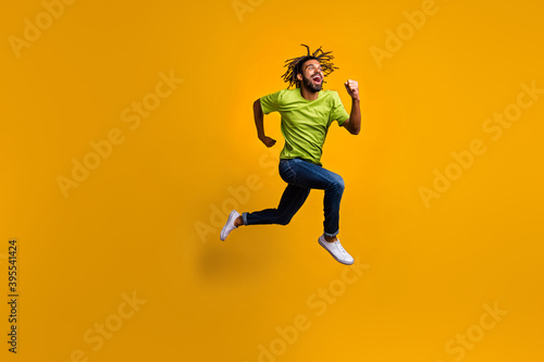 Full length photo portrait of excited runner jumping up isolated on vivid yellow colored background