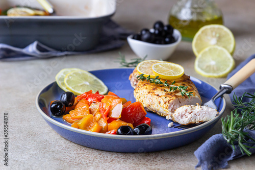 Oven baked or grilled chicken breast with baked bell pepper, lemon and olives, light concrete background. Healthy food.