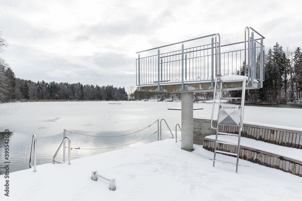 Strandbad im Winter mit schneebedecktem Sprungturm über zugefrorenem See Strandbad im Winter mit schneebedecktem Sprungturm über zugefrorenem See