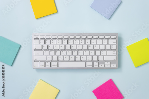 White Portable Computer Keyboard Keys or Keyboard Button and Colorful Stick Note or Note Pad on Blue Pastel Minimalist Background
