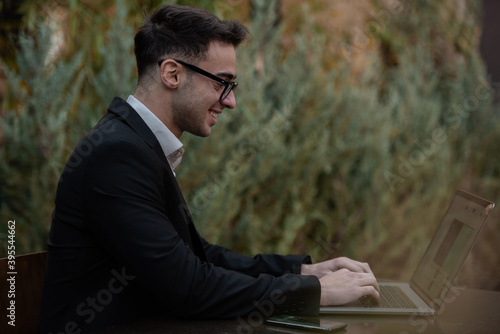 Young successful businessman working on a laptop while sitting in coffee bar during work break lunch. Speaking on his phone while working and drinking coffee.