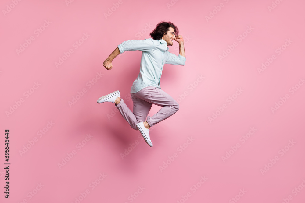 Full size profile side photo of young excited man jump wear purple trousers white shoes look copyspace isolated on pink color background Full size profile side photo of young excited man jump wear purple trousers white shoes look copyspace isolated on pink color background