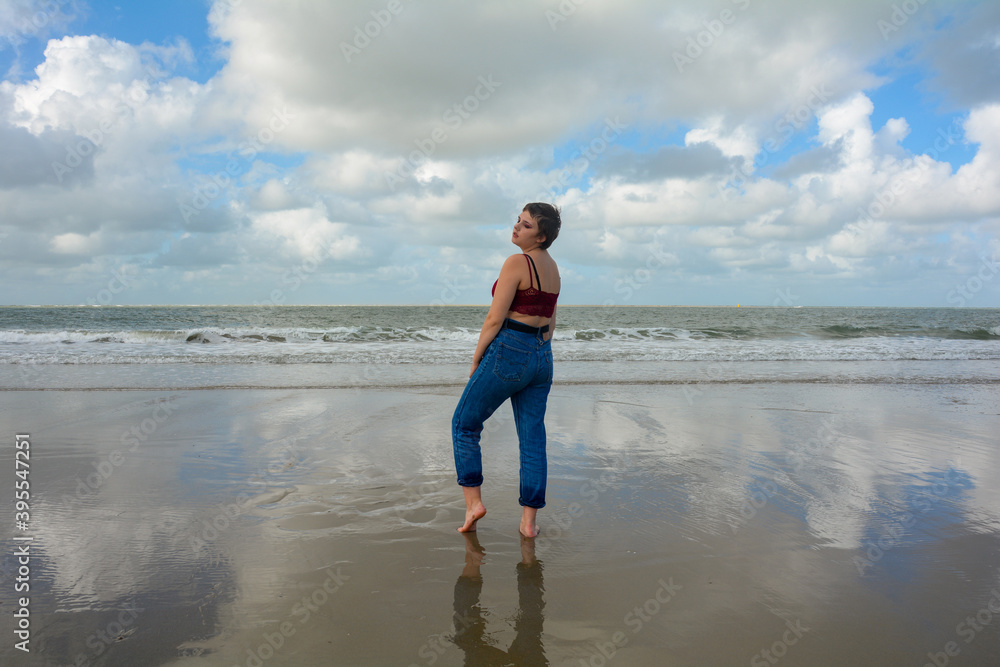 Sensual young woman, standing sideways on the beach in front of the sea Sensual young woman, standing sideways on the beach in front of the sea
