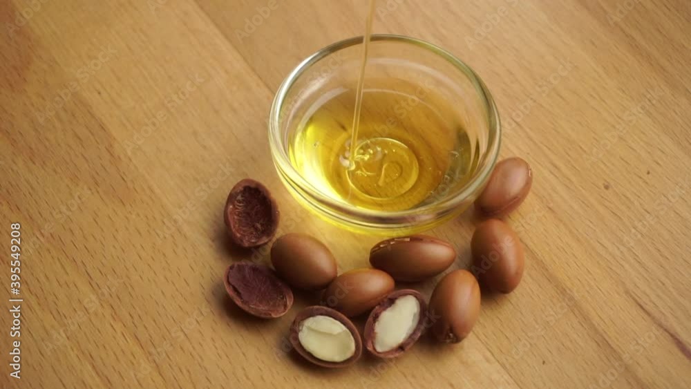 Argan oil into a glass bowl with argan seeds on a wooden background. Argan oil based cosmetics concept. Argan oil into a glass bowl with argan seeds on a wooden background. Argan oil based cosmetics concept.