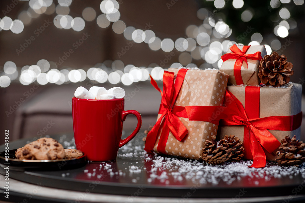 Hot coffee mug with sweets, gifts and pine cones on the table, gold background with white garlands Hot coffee mug with sweets, gifts and pine cones on the table, gold background with white garlands