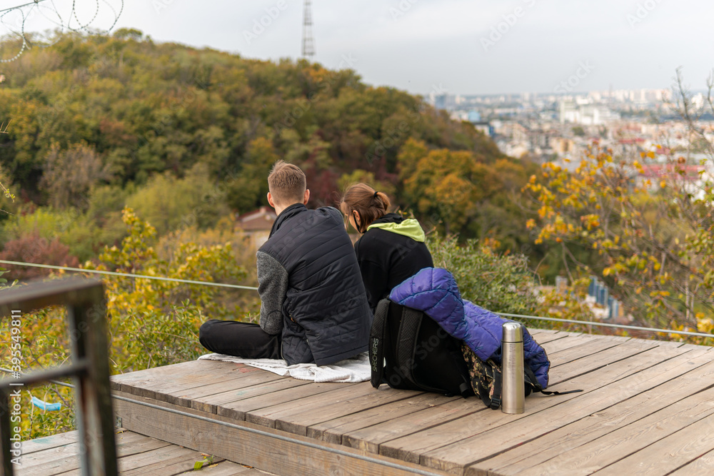 A sweet lovely couple enjoys time together on the observation deck with thermos, looking at the city and autumn nature A sweet lovely couple enjoys time together on the observation deck with thermos, looking at the city and autumn nature