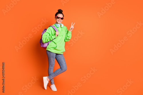 Photo of charming young lady dressed green sweatshirt backpack eyewear showing v-sign isolated bright orange color background