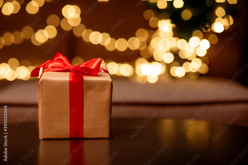 Gift box with a red bow on a brown table with flickering lights bokeh background. Gift box with a red bow on a brown table with flickering lights bokeh background.