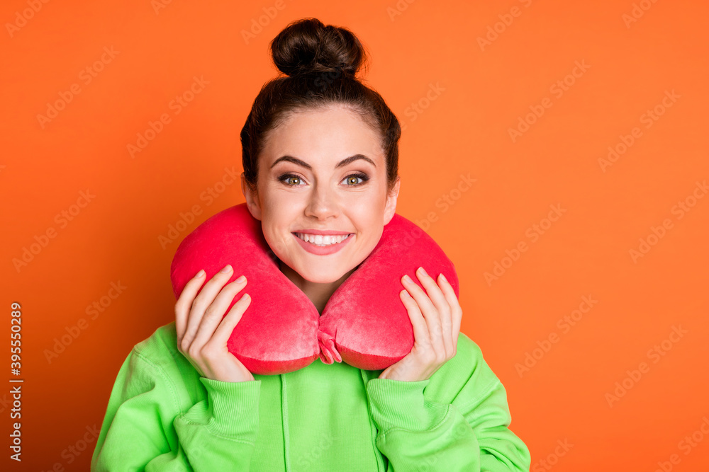 Photo of adorable young woman wear green hoodie neck pillow smiling isolated vivid orange color background Photo of adorable young woman wear green hoodie neck pillow smiling isolated vivid orange color background