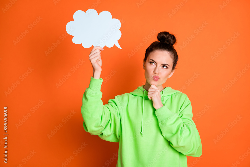 Photo of cute doubtful young lady dressed green sweatshirt brainstorming looking paper cloud isolated bright orange color background Photo of cute doubtful young lady dressed green sweatshirt brainstorming looking paper cloud isolated bright orange color background