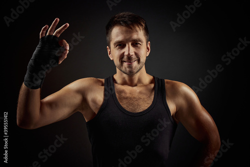 Handsome fit smiling bearded man showing Ok gesture on black background