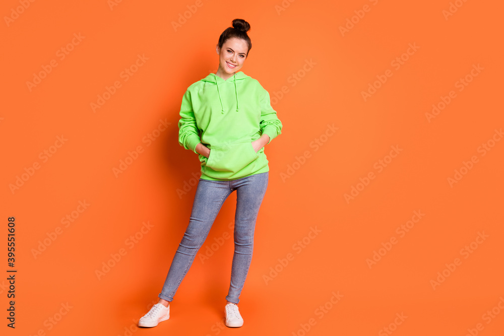 Full length photo portrait of girl with hands in pockets isolated on vivid orange colored background with blank space Full length photo portrait of girl with hands in pockets isolated on vivid orange colored background with blank space