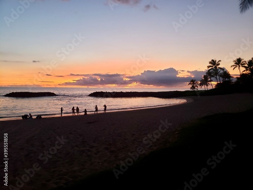 people walk along the coast during sunset on a sandy beach in Hawaii