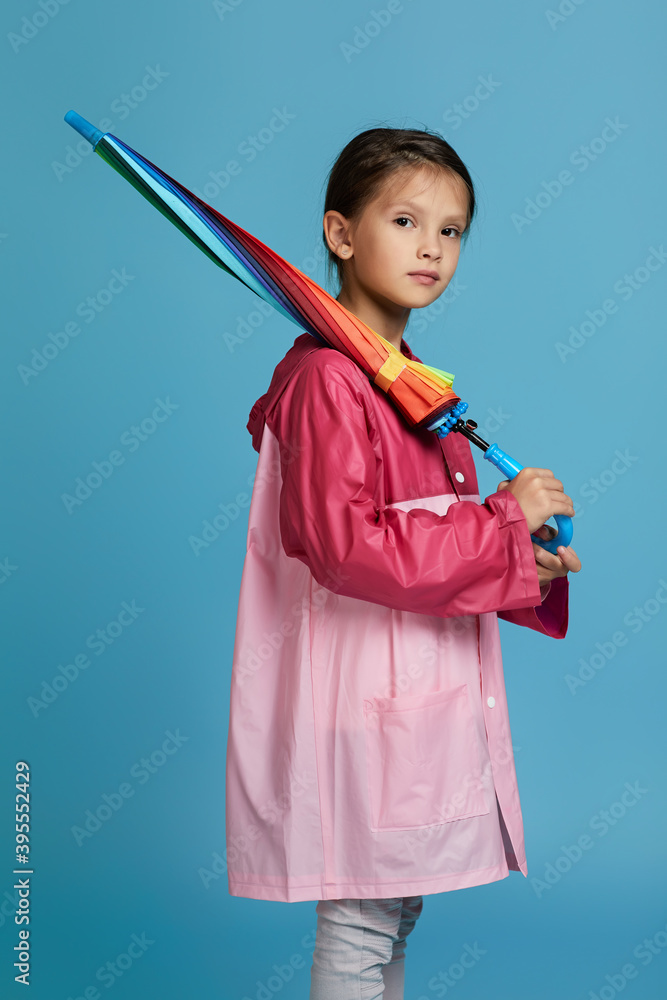 cute child girl with multicolored umbrella in pink rain coat on blue background. autumn mood cute child girl with multicolored umbrella in pink rain coat on blue background. autumn mood