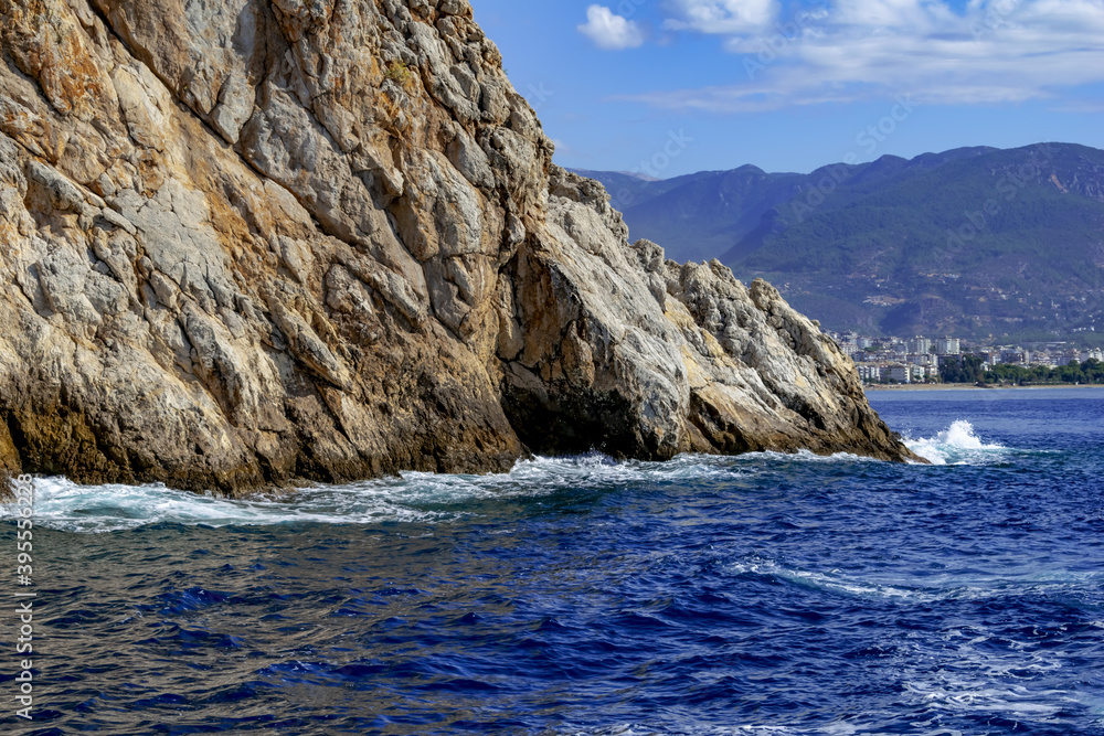 Rock in the Mediterranean Sea against the backdrop of a panorama of Alanya (Turkey). Waves beat against a stone mountain and a town on the coast on the horizon Rock in the Mediterranean Sea against the backdrop of a panorama of Alanya (Turkey). Waves beat against a stone mountain and a town on the coast on the horizon