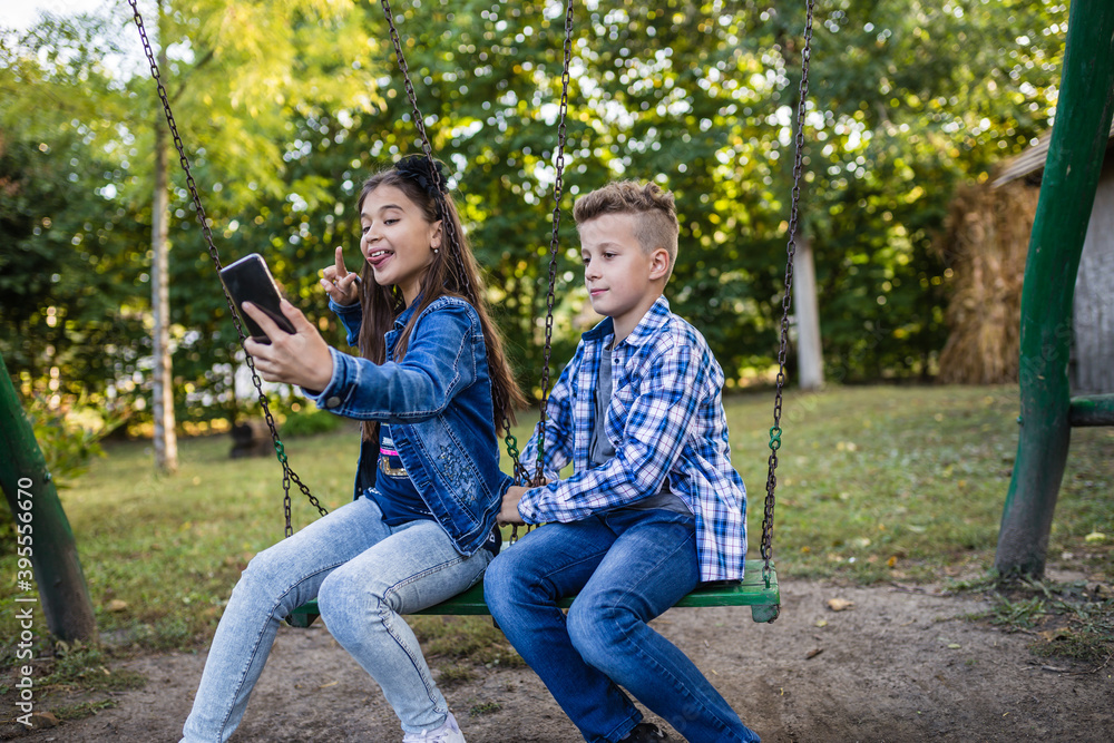 Kids taking selfie with mobile phone while sitting on swing Kids taking selfie with mobile phone while sitting on swing